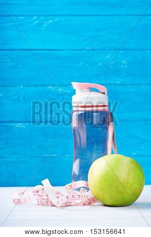 Fitness concept with water, measurement tape and fresh apple on a blue background