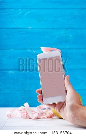 Women takes photo with smarphone with empty screen. Water and measurement tape - diet and sport eating concept. On a wooden background. Shooting for social media