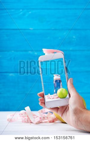 Women takes photo with smarphone fitness concept on a screen. Fresh apple, water and measurement tape - diet and sport eating concept. On a wooden background. Shooting for social media