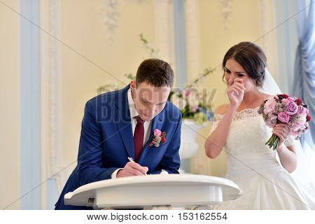 Beauty bride and handsome groom are registering the marriage. Wedding couple is marrying. Beautiful model girl in white dress and in lace veil. Man in suit. Female and male portrait. Cute lady and guy