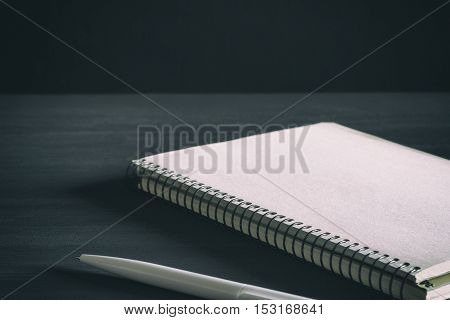 Single simple empty white notebook with a blank for drawing or writing and white plastic pen are on a Desktop from black chalkboard. Mockup. Toned and grained