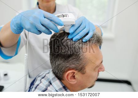 diagnostics hair and scalp. Trihoskopiya. Doctor examine patient male hair a special apparatus