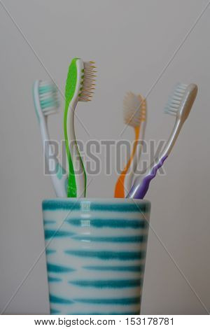 Four different colored toothbrushes in the ceramic bowl facing each other