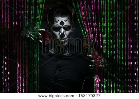 Portrait of a man with a mexican calaveras makeup looking through the curtain