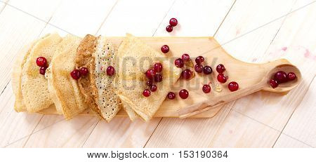 pancakes folded triangles on a wooden board with cranberries and honey. Shrovetide. day pancakes