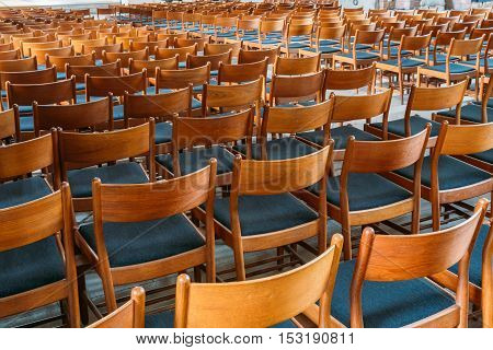 Many Empty The Same Wooden Chairs With Backrest And Blue Upholstery Standing In Neat Rows In Large Auditorium.