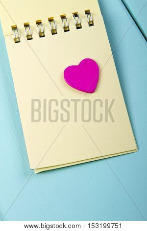 wooden pink heart and a notebook on a spring on a wooden turquoise background. vertical shot. love notes