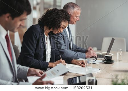 Diverse group of focused businesspeople working while sitting in a row together at a table in an office boardroom