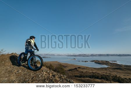 Fatbike also called fat bike or fat-tire bike - Cycling on large wheels. Traveller cyclist stands on the top of the mountain. He is resting on a trip looking at the sunset and sitting on the bike.