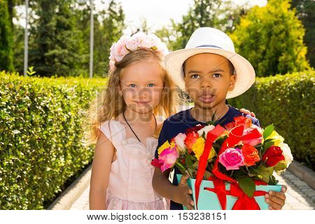 Black african american boy kid gives flowers to girl child on birthday. Little adorable children in park. Childhood and love.