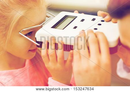 health care, medicine, people, eyesight and technology concept - close up of optometrist with pupillometer checking patient intraocular pressure at eye clinic or optics store