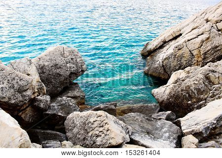 Blue sea or ocean water washes stones or rocks of coast beach seashore on sunny day on seascape background