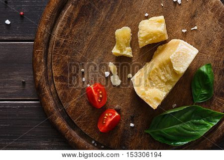 Cheese delikatessen closeup on rustic wood. Wooden desk with parmesan, camembert cuts decorated with garlic, tomato and basil, top view image
