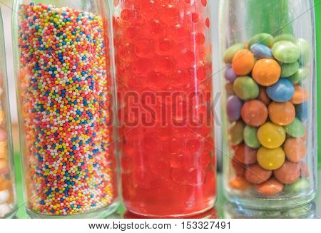 horizontal image of little bottles of assorted decorative christmas candy sprinkles standing in a row on a red book adorned with pine cones and cranberries on burlap background