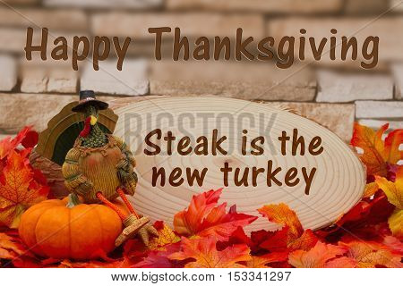 Funny Happy Thanksgiving message Some fall leaves turkey on a pumpkin and wood plaque on weathered brick with text Happy Thanksgiving steak is the new turkey