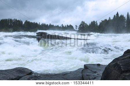 Cascades of water in the big river. Rocks and cliffs break the speed. Forests both sides.