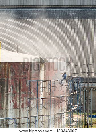Worker cleaning storage tank by air pressure sand blasting in high position.