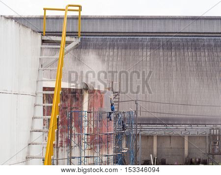 Worker cleaning storage tank by air pressure sand blasting in high position.