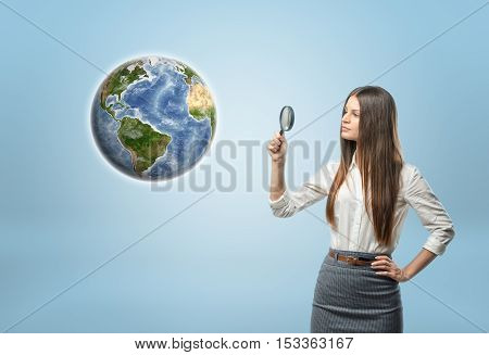Full portrait of businesswoman looking at Globe Earth through a magnifier. Environment and ecology. Resource usage. Find useful resources. Search to benefit from natural resources. Elements of this image are furnished by NASA.