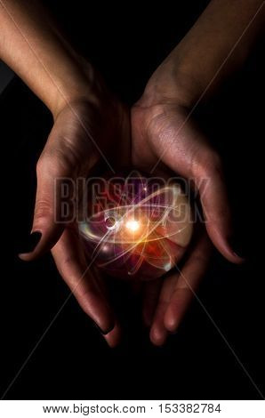Female hands hold crystal ball with atom particle for fortune telling background