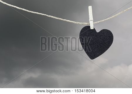 Black Heart paper hanging on a brown hemp rope on rain clouds background Concepts about unrequited love and heartbreak.