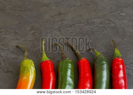 hot redgreen and orange chilies in a row on a dark grey background