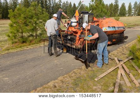 Colbert, WA - October 24, 2016: Workers from Black Diamond Asphalt Paving, LLC., repairing patches and re-paving a private road/driveway