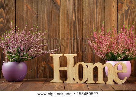 Heathers in ceramic pots and the letter 'home' against dark wooden planks