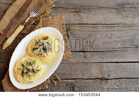 Pasta with champignons, cheese and dill on a plate, fork, knife on old wooden background with empty copy space for text. Delicious pasta nests with filling. Top view