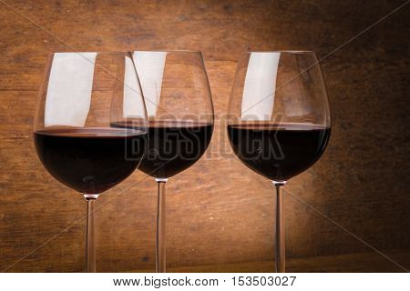 Three fine wine glasses half full with liquid over brown wooden background with spotlight effect
