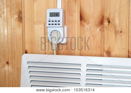 Working white electric convector heater plugged to timer power socket operated in smart house system against wooden wall inside room side view closeup