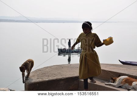VARANASI, UTTAR PRADESH, INDIA - FEBRUARY 17, 2016 - Unidentified indian kid walking on the ghats in Varanasi with a monkey following her and holy river Ganga on the background