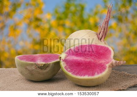 One whole and sliced watermelon radish on a wooden table with blurred garden background.