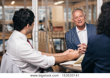 Mature businessman talking with young staff members while sitting together at a table in an office boardroom