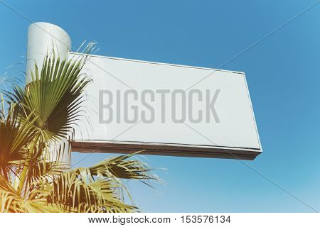 Mock up of blank white advertising billboard in Dubai with clear blue sky behind it and palm in front of it