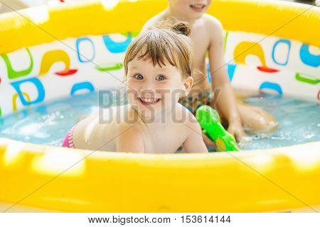 Little Girl Bathes In Yellow Inflatable Swimming Paddling Pool Outdoors