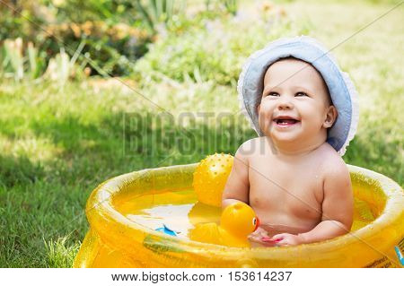 Beautiful Baby Girl In Cotton Panama Cap Bathes In Yellow Inflatable Swimming Paddling Pool