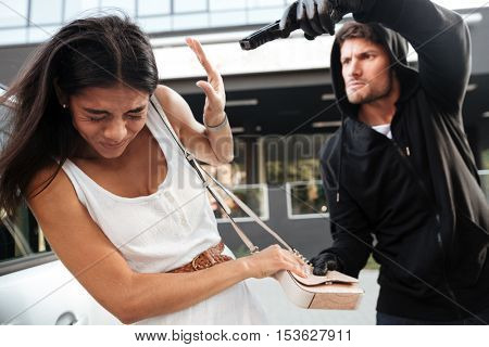 Aggressive young man with gun trying to steal purse of frightened young lady on the street
