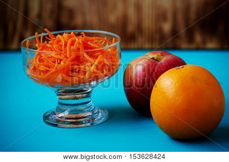 Grated carrot in a glass Cremant, on a blue background with an Apple and orange