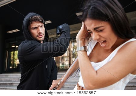 Man thief with gun attacking scared young woman on the street