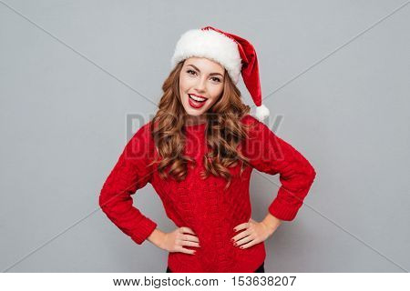Smiling attractive young woman in santa hat and red sweater over gray background