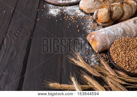 Bread sorts border on wood with copy space background. Brown and white whole grain loaves still life composition with wheat ears scattered around. Bakery and grocery food store concept.