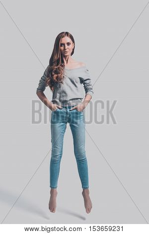 Beauty in mid-air. Mid-air shot of attractive young woman in casual wear holding hands in pockets and looking at camera