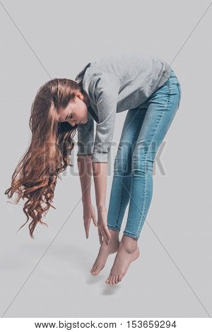 Mid-air beauty. Mid-air shot of attractive young woman in casual wear bending in front of grey background