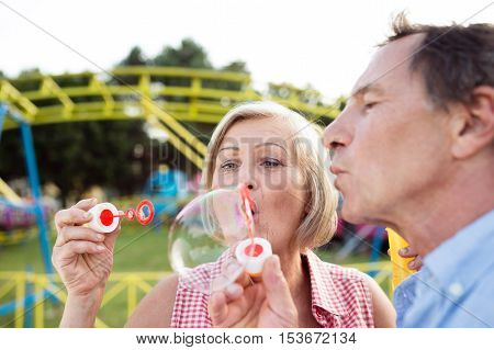 Senior couple having a good time at the fun fair, blowing soap bubbles with bubble wand.
