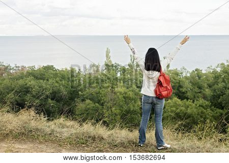 Young girl (brunette) and jeans with a red backpack looking out to the sea. Selective focus.