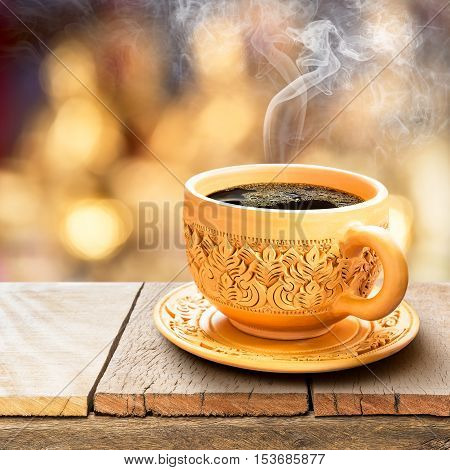 Black coffee in traditional thai art engrave cup with smoke on wooden table