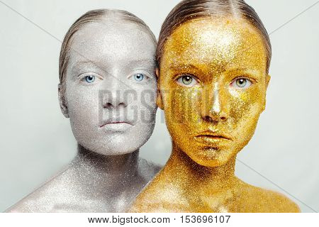 Beautiful amazing portrait of two woman. Unreal make up like a space. Closeup shooting in studio with silver background. Emotion posing of model. gold silver glitter.