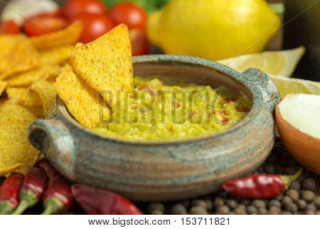 Guacamole in home crafted bowl with tortilla chips and chilli around.