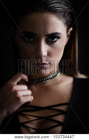 Closeup portrait of a young trendy agressive woman in bodysuit posing near black wall